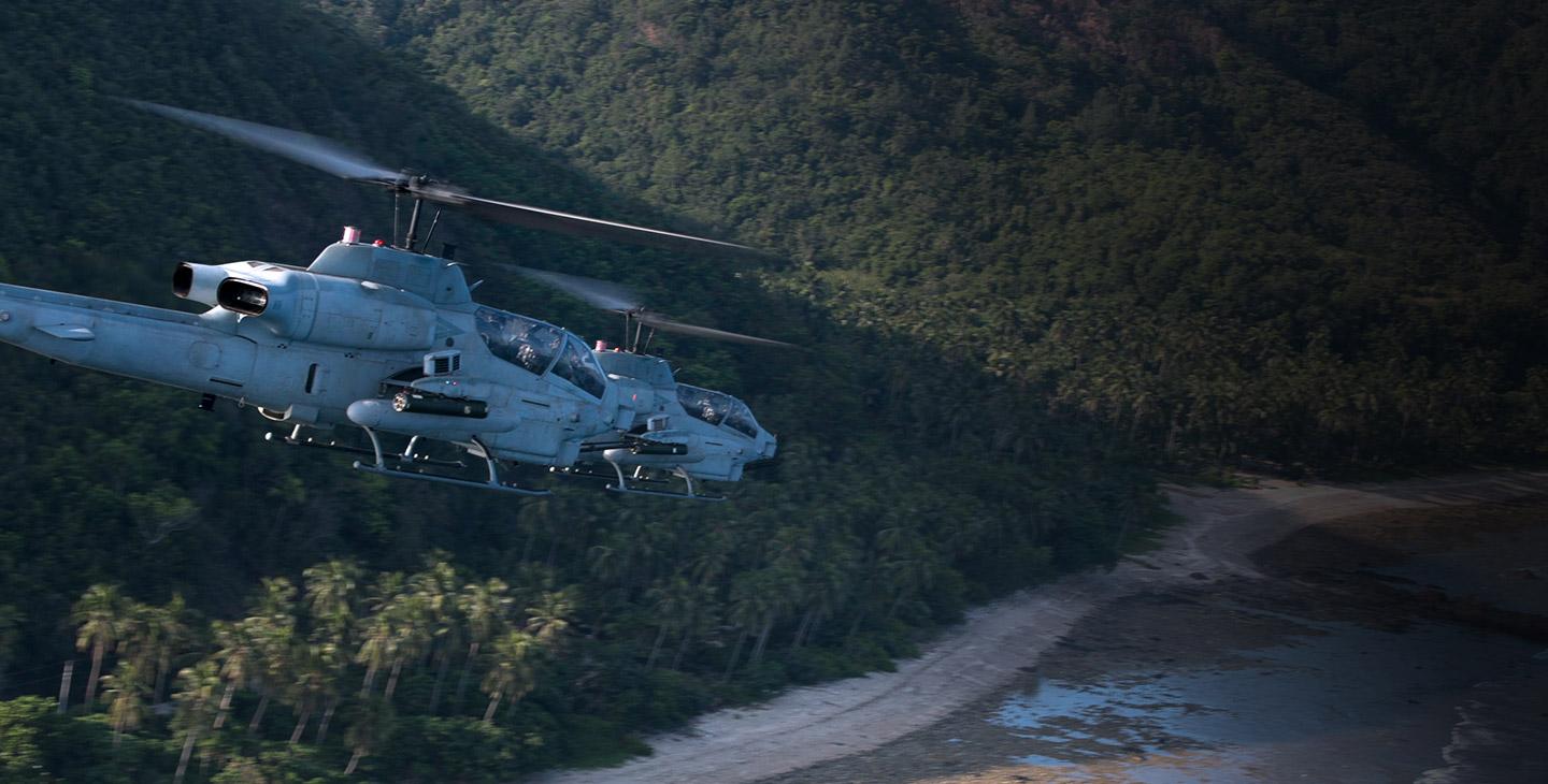 Two military helicopters flying over a coastline
