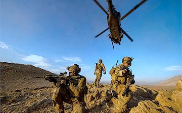 Three soldiers on watch out in the field with a helicopter flying above